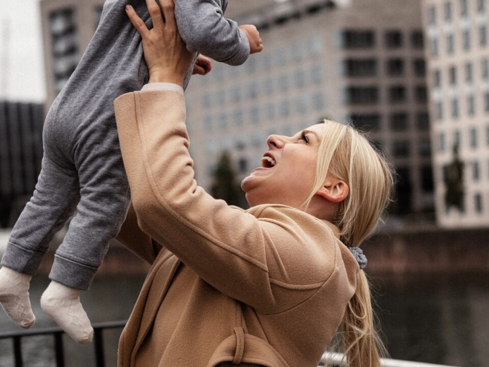 Mama unosząca roześmiane niemowlę, w tle miasto nad rzeką